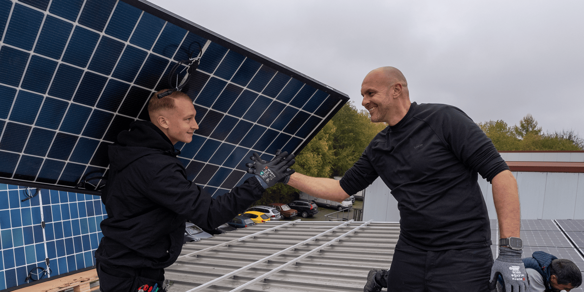 2 Arbeiter geben sich die Hand vor einer Solarzelle